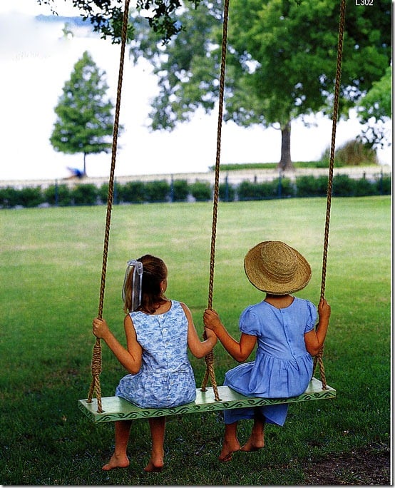 Double swing hung from tree with two girls on it.
