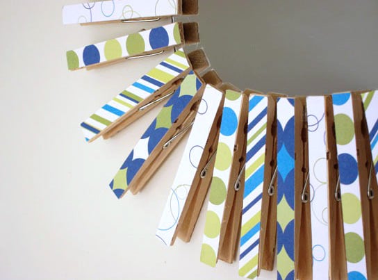 Scrapbook paper covered clothespins creating a frame on a round mirror