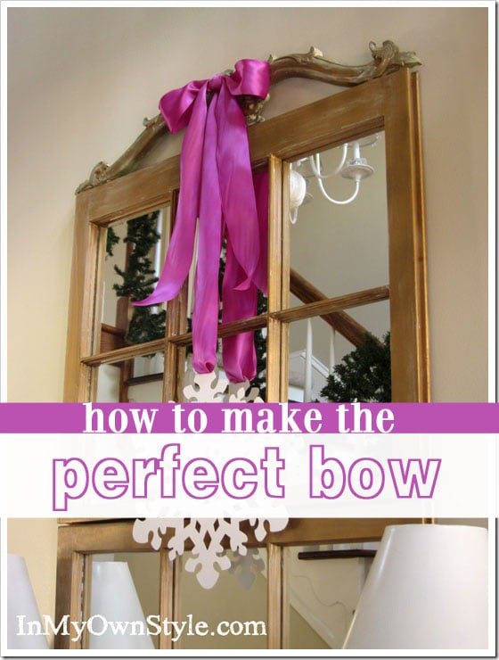 Pink bow attached to long gold mirror on wall. 