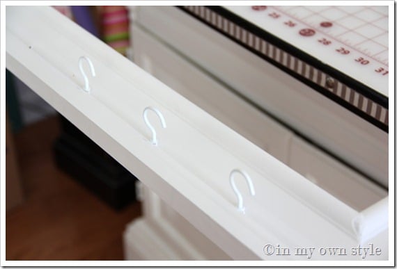 3 white cup hooks screwed into a white frame.