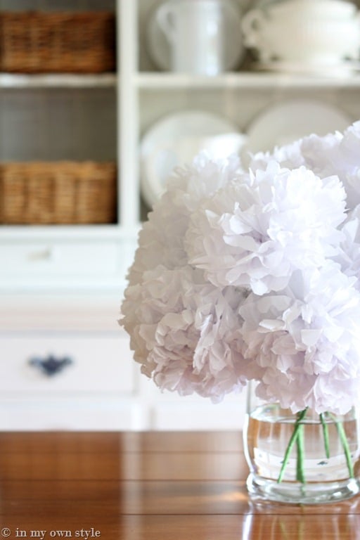 Close up of tissue paper flowers in glass vase on dining table.