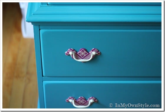 Purple napkin covered drawer pulls on a turquoise painted chest of drawers.