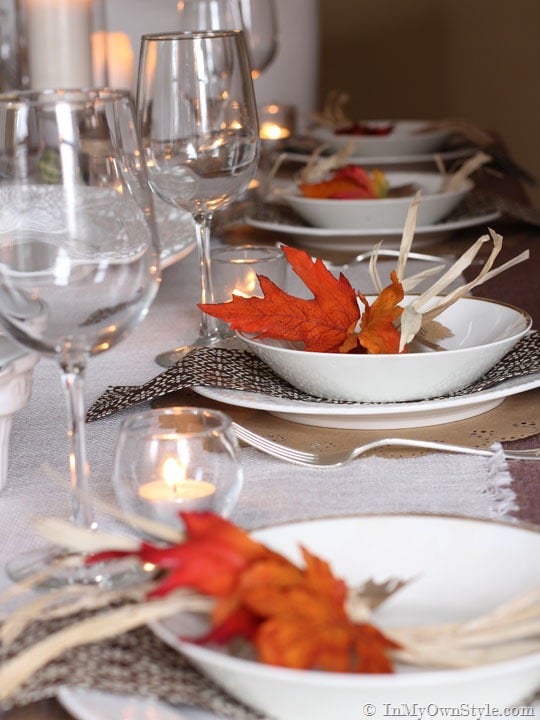 Thanksgiving table setting with wine glasses, white plates and orange and brown accents.