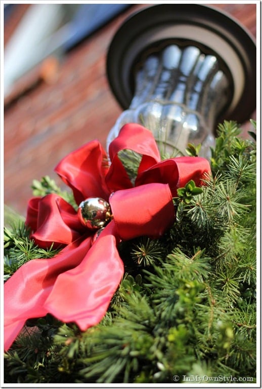 Outdoor house lights decorated for Christmas with red ribbon and pine greenery.