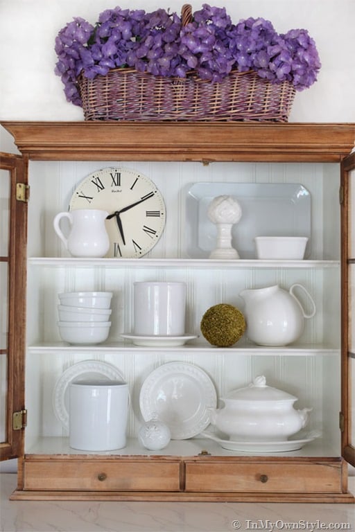 Open kitchen cabinet styling idea using white dish ware, pitchers and decorative accessories.