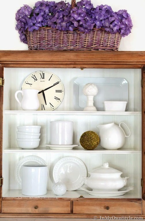 White dishes and Roman numeral clock in cabinet