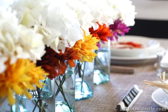 Mason jars lined up in the center of a dining table are used a fall flower vases. 