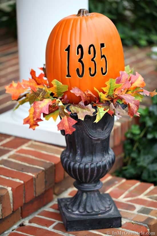 Pumpkin with carved house address number on garden urn on porch.