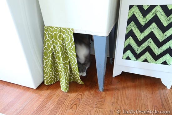 Half of a fabric skirt attached to laundry room sink to begin to hide a cat litter box in a laundry room.