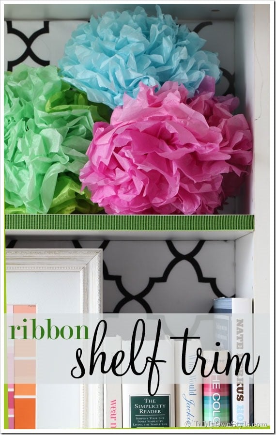 Bookcase shelf with ribbon trim and colorful tissue paper flowers on the shelves.