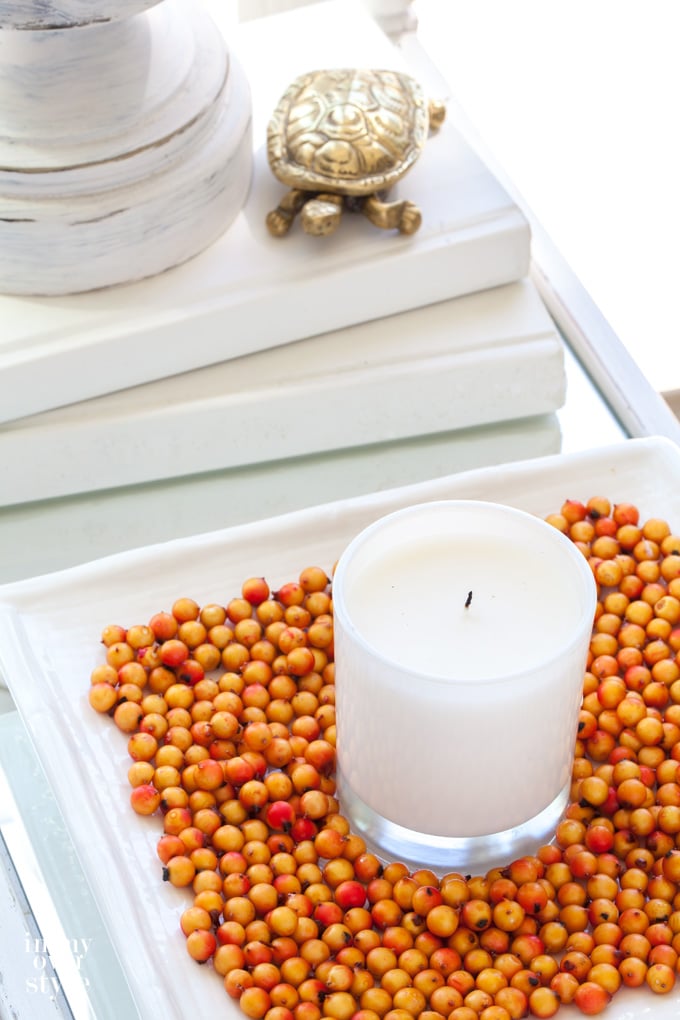 Candle on white square tray with orange beans.