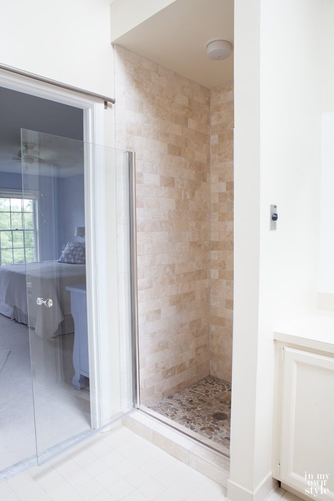 Master-bathroom-decorating showing completed tumbled stone tile makeover. Glass shower door is open.