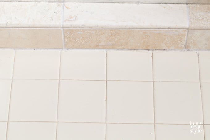 Stone-tile-shower floor next to beige tile on bathroom floor.