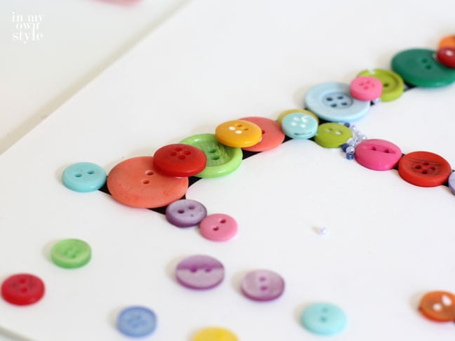 layering colorful buttons on a printed letter to create wall art.