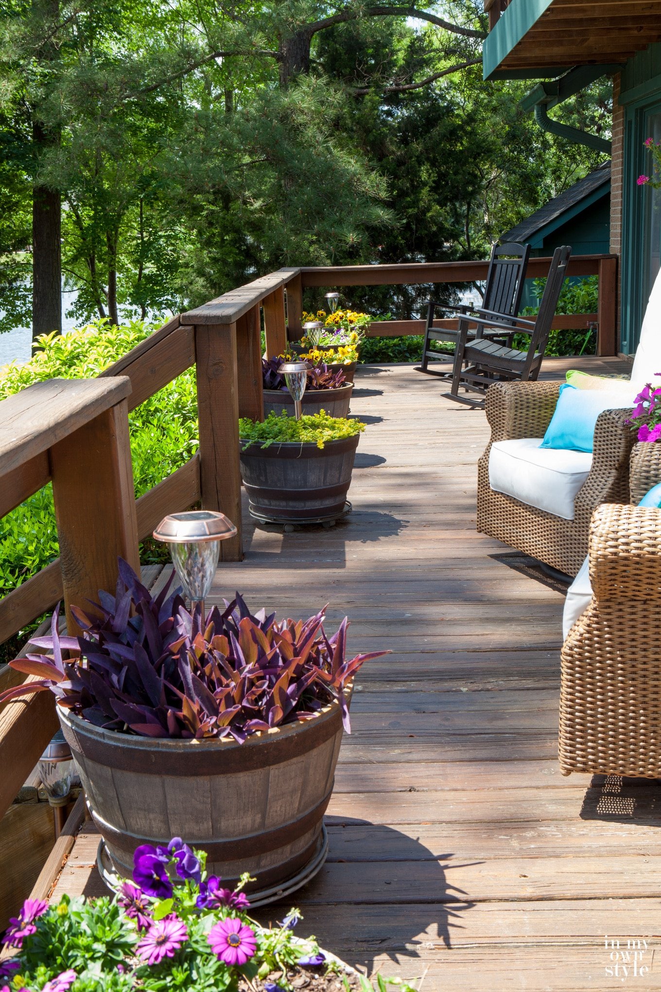 View of deck lined with barrel style planters with outdoor solar lights in each.