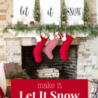 A white mantel on a stone fireplace decorated with white signs that say Let it Snow