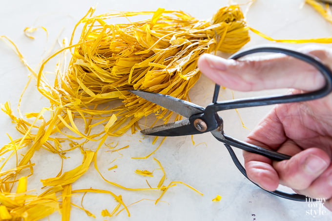 cutting bottom end of raffia tassel with scissors