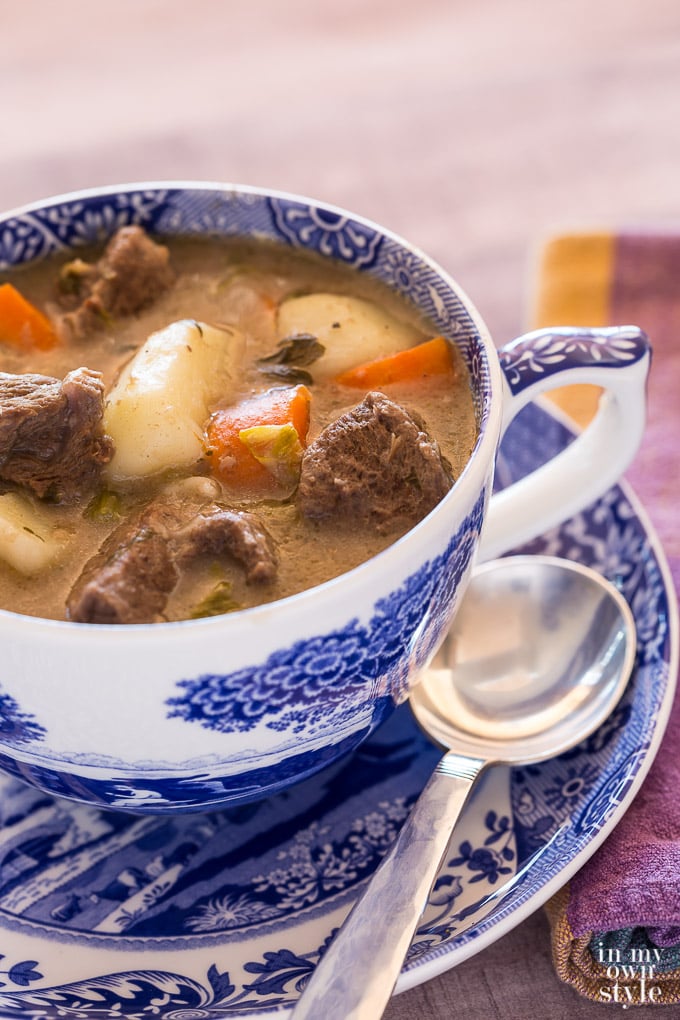 Jumbo blue and white cup and saucer filled with beef stew. Spoon resting on saucer.