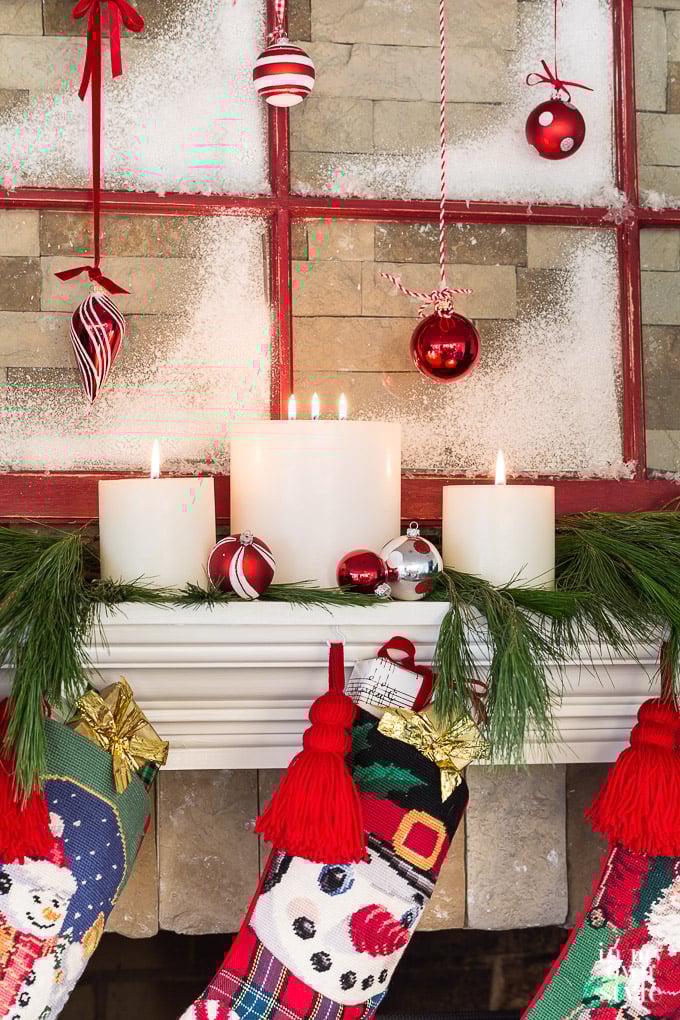 Red yarn tassels attached to Christmas stockings hanging from a fireplace mantel
