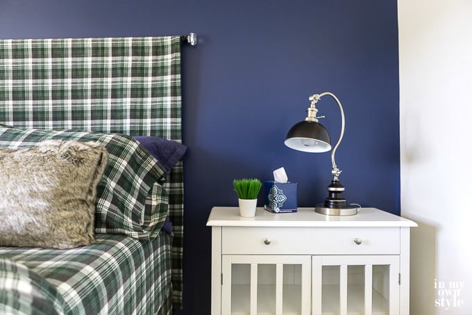 Blue accent wall in bedroom. Bed has a green black and white checked headboard and sheets. 