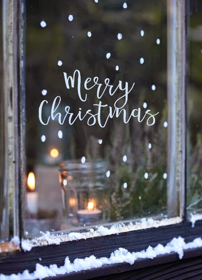 Merry Christmas written on a snowy window with a candle inside.