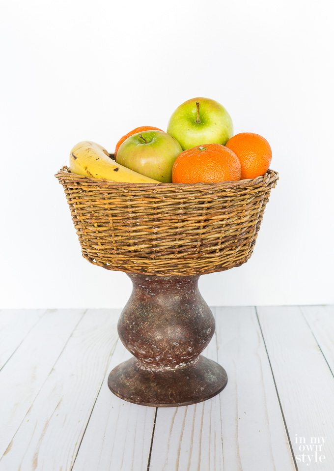 a basket filled with fruit on top of a pillar candle holder