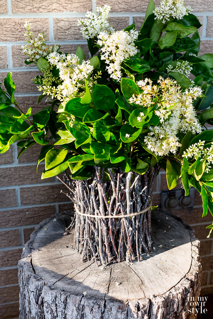 A rustic DIY twig vase on a tree trunk side table