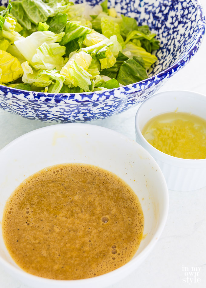 3 bowls - a blue and white one filled with lettuce, one with dressing and a small one with garlic oil.