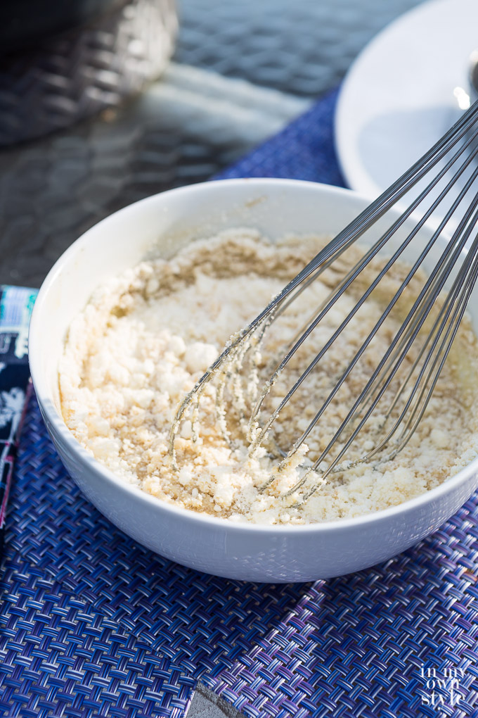 Whisking cheese into dressing that is in a white bowl.