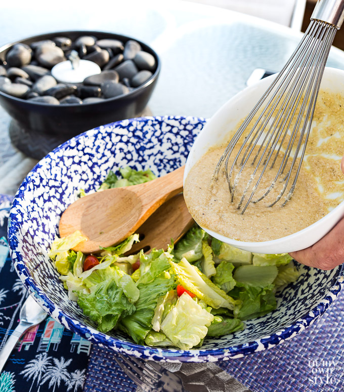 Whisking dressing over lettuce in big bowl.
