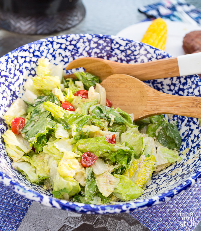 Caesar Salad in blue and white speckled bowl with wooden spoon and fork ready to be served.