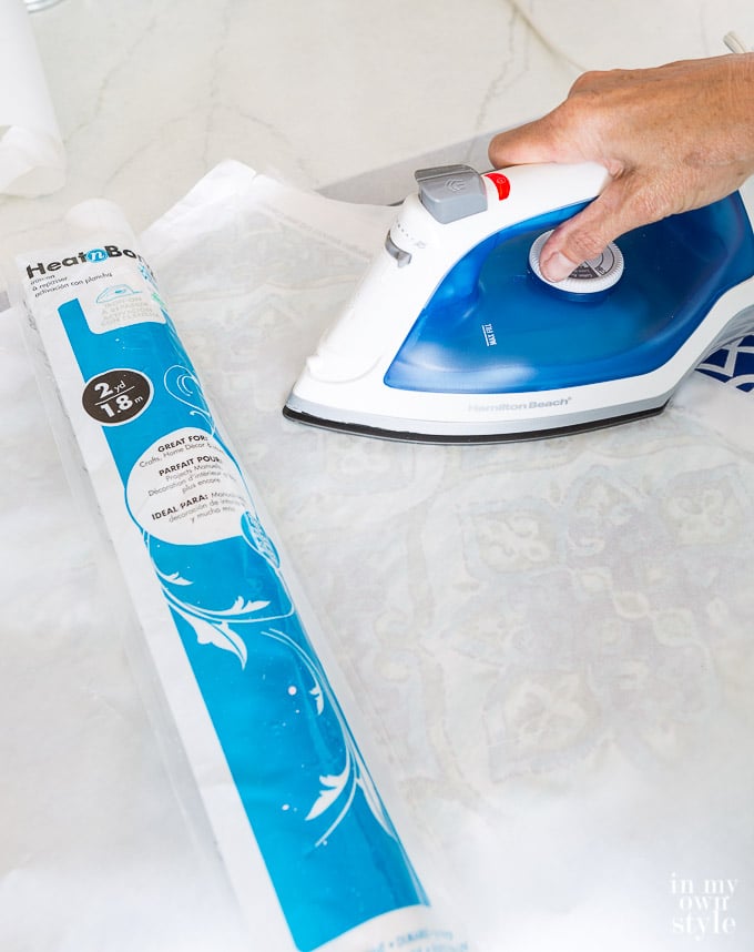 Using an iron to press heat n bond vinyl onto fabric.