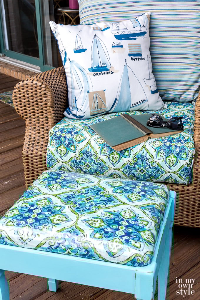 Close up of newly covered stool next to rattan rocker. The fabric on the stool matches the cushion on the rocker.