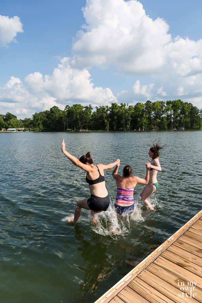 3 girls holding hands while jumping onto a lake from a dock.
