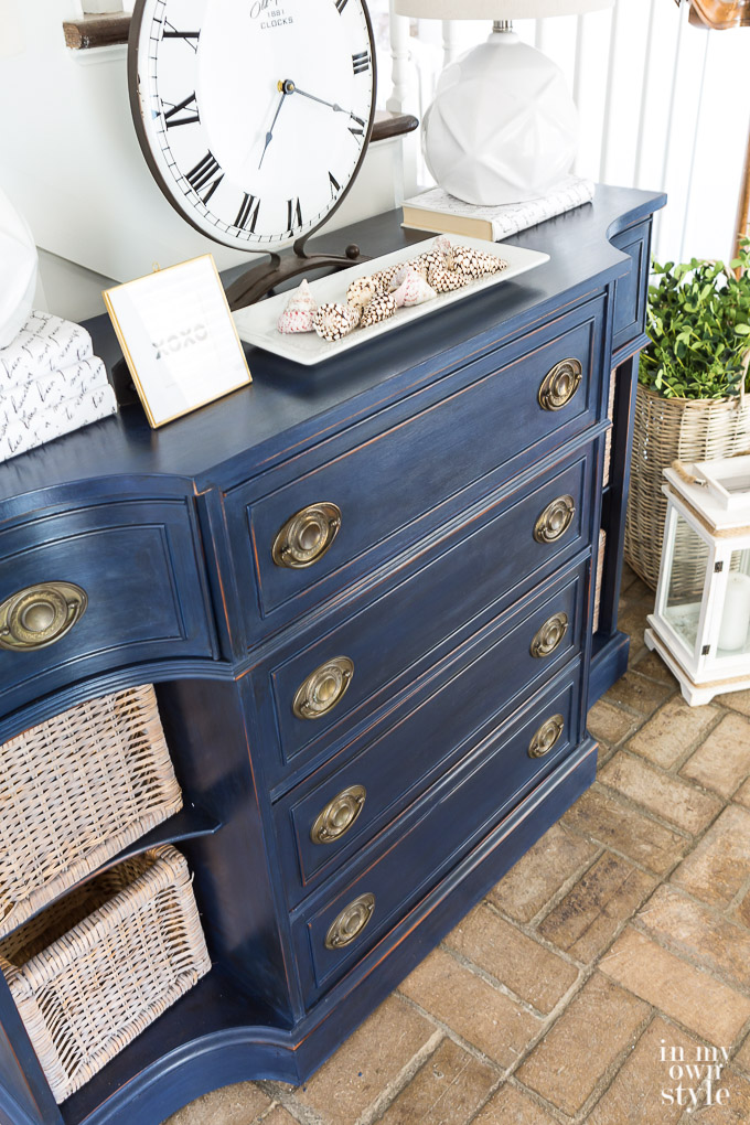 Blue painted sideboard with decorative accessories on top and baskets on shelves.