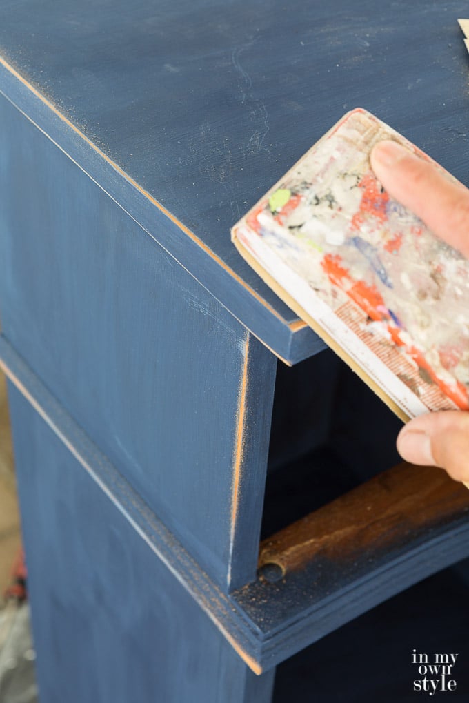 Sanding the edge to distress a piece of painted furniture.