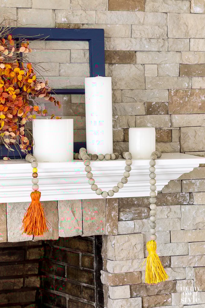 3 white candles on mantel with wood garland wrapped around them