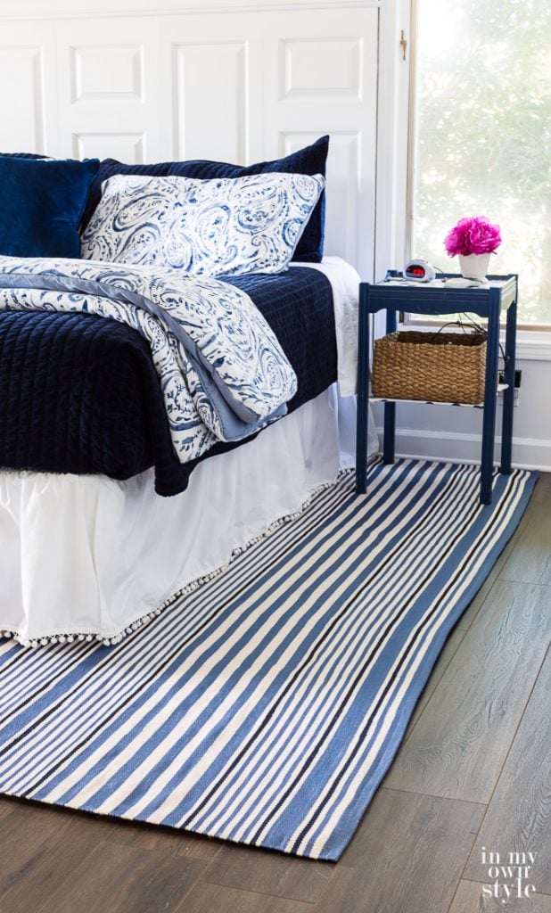 Blue and white bedroom with blue and shite striped area rug over dark hardwood floor.