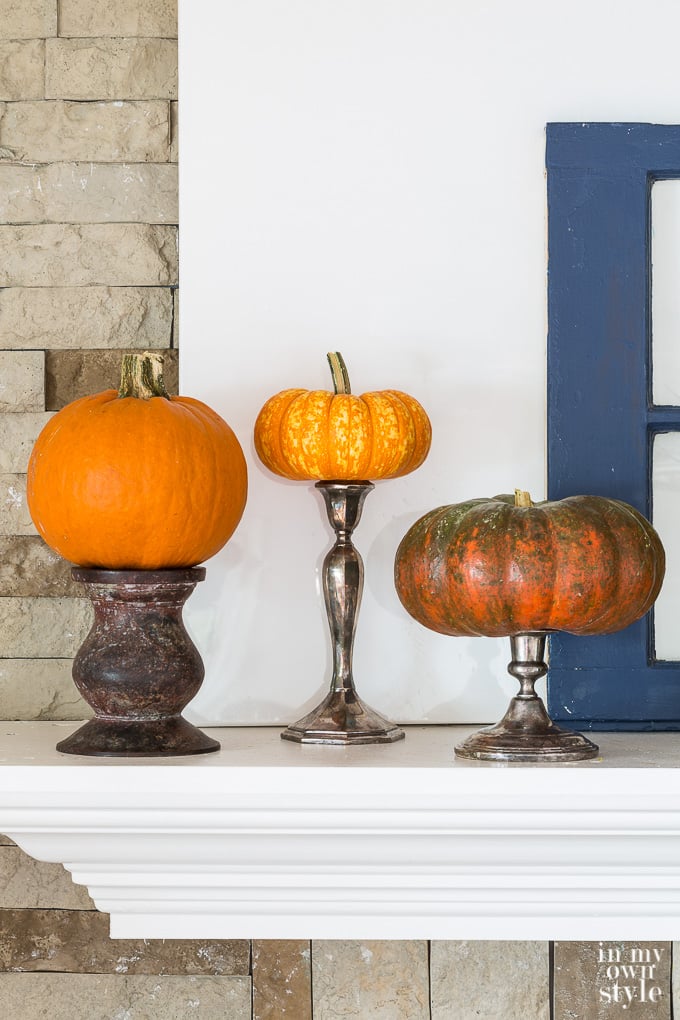 Pumpkins on a mantel raised on candle holders and candlesticks