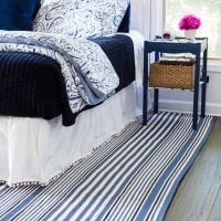 Blue and white decorated bedroom with blue and white striped area rug under the bed.