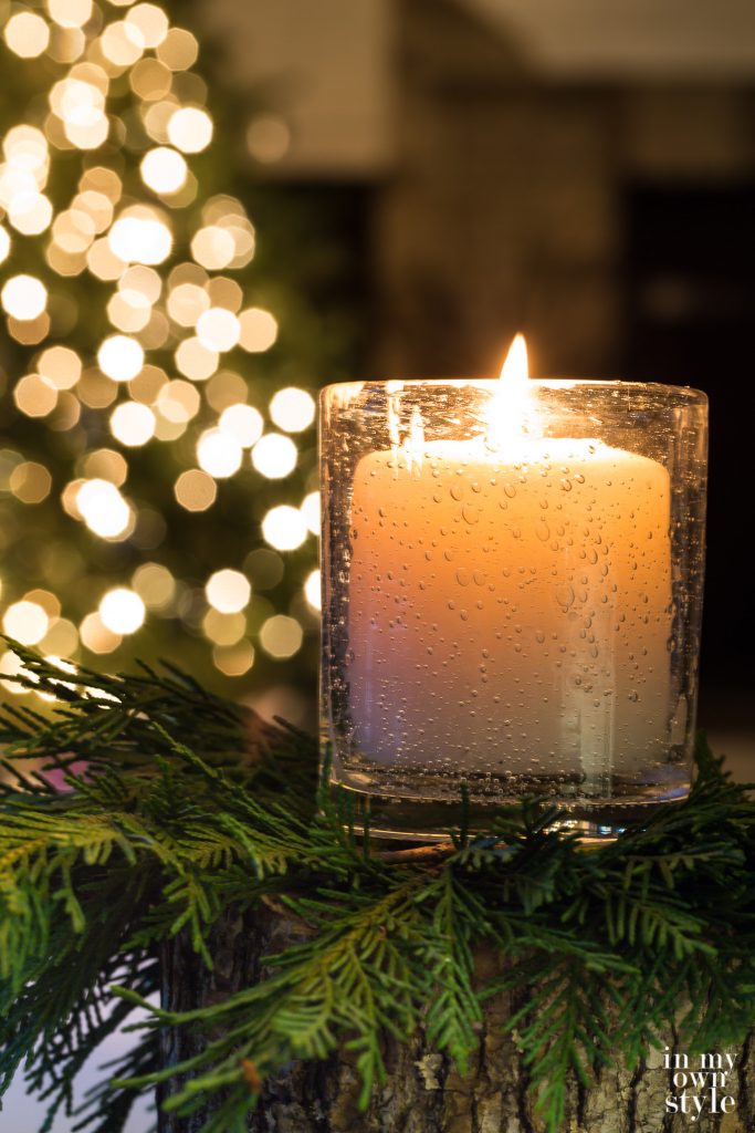 Candle glowing in front of a Christmas tree with white lights