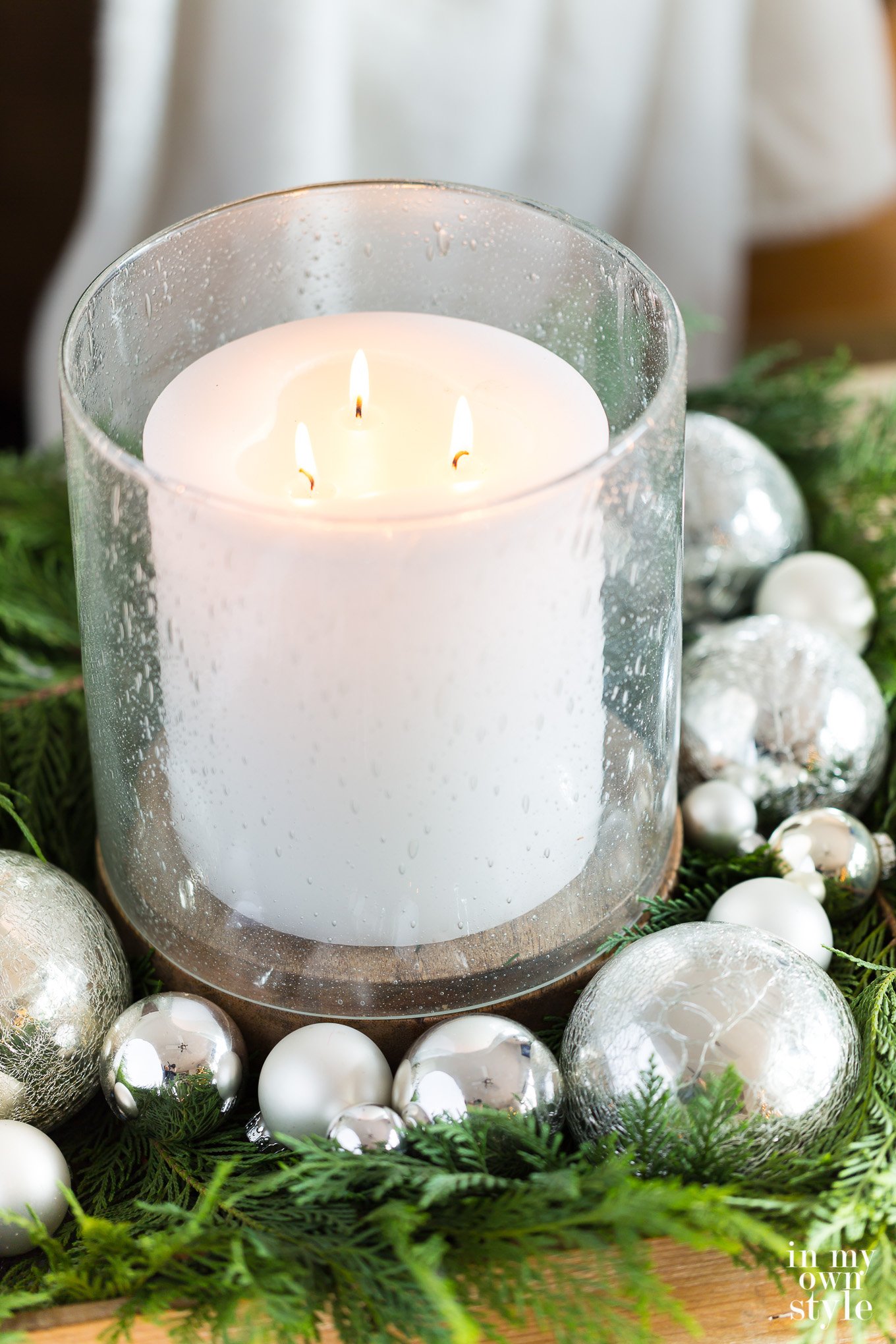 Bubble glass hurricane and large white candle table decorated for Christmas.