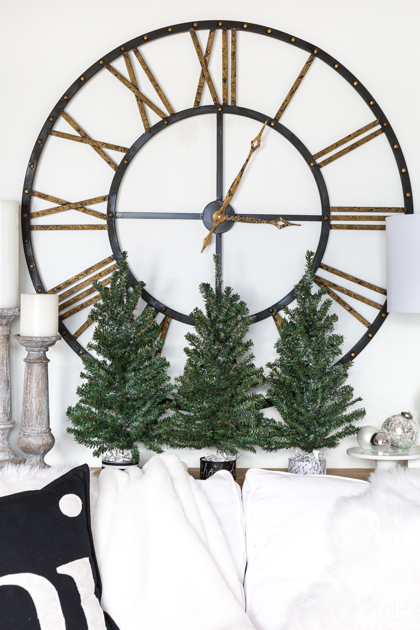3 pine trees on sofa table with a large metal clock behind it.