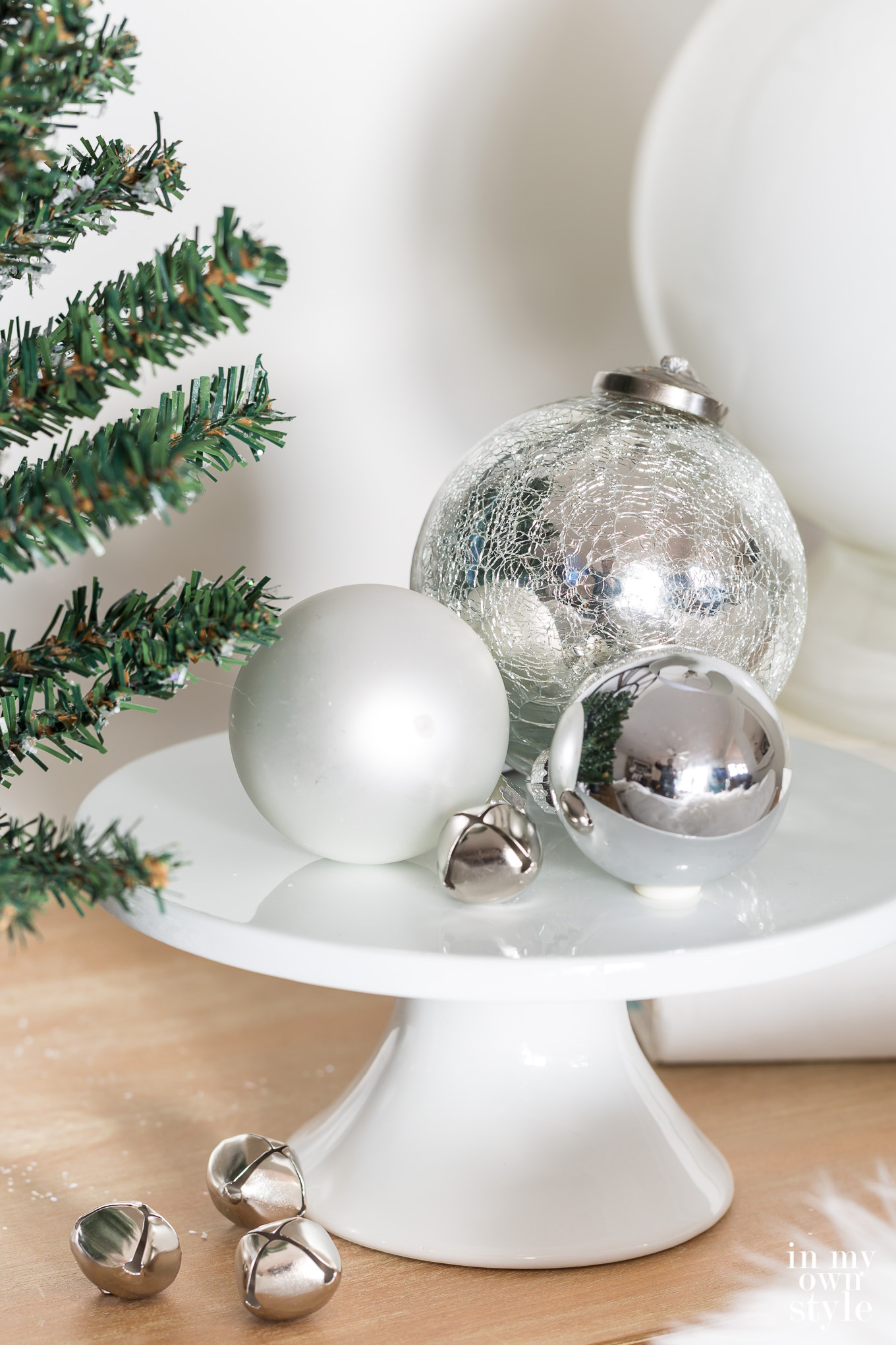 Shiny silver Christmas ornaments on white pedestal.