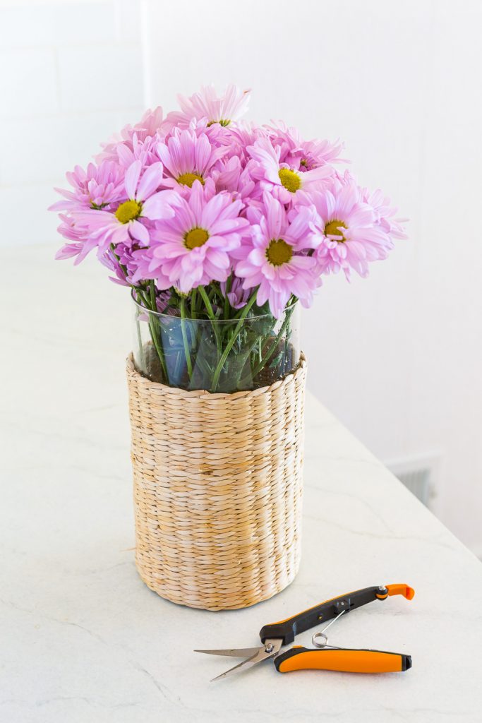 Pink flowers in a wicker and glass vase.
