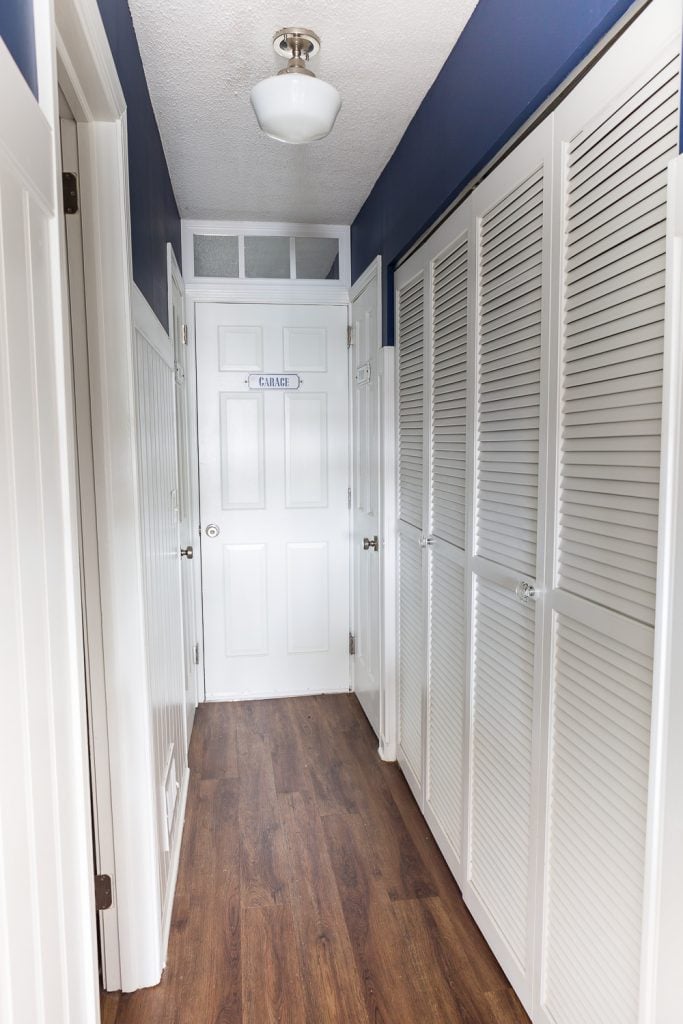 Dark hallway decorating idea. White vertical paneling on lower 3/4 of wall and navy blue wall paint on top. White doors with handmade signs on them telling what is behind each door.