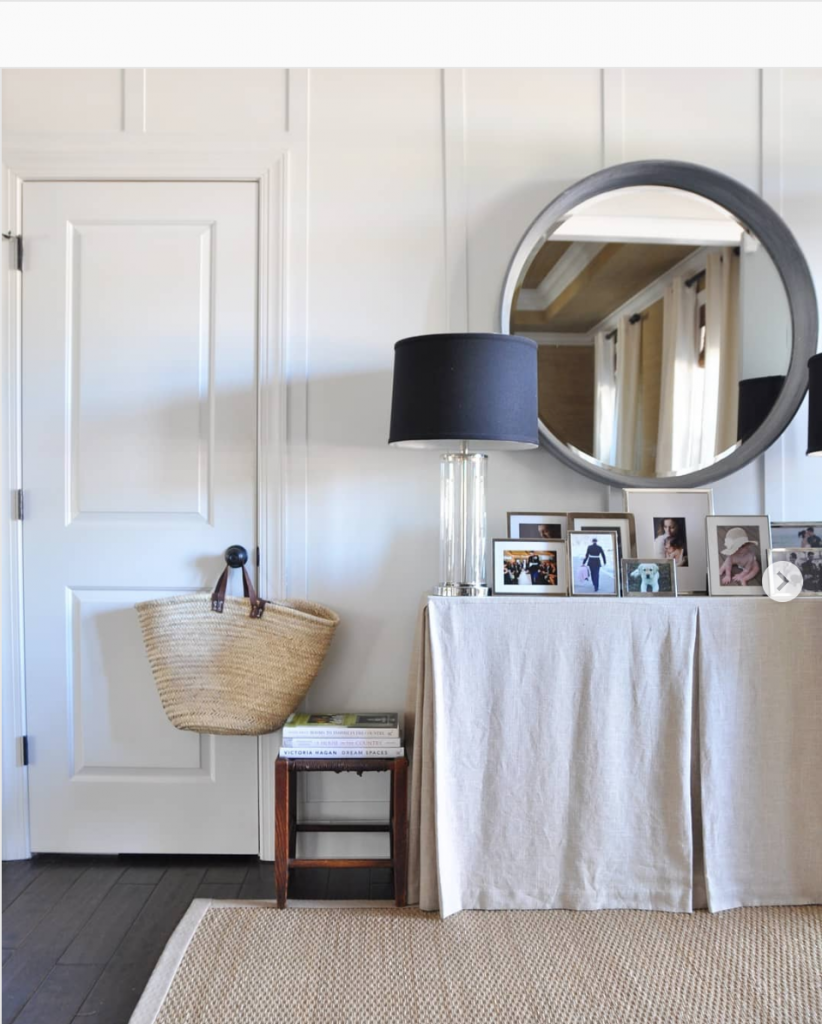 A linen covered console table in white paneled room with seagrass rug.