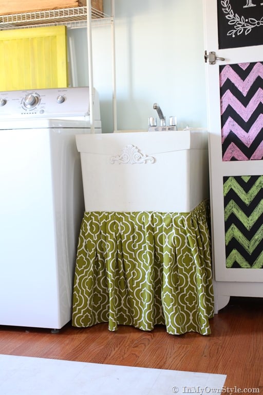 Laundry room where laundry tub has a skirt of fabric around it to hide clutter or in this case a cat litter box.