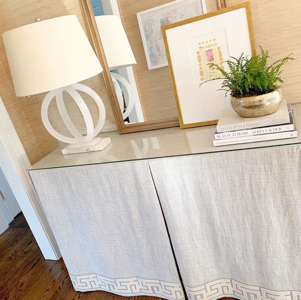 A white linen skirted console table with glass on top.