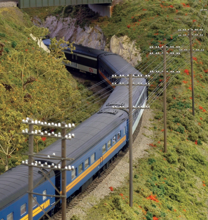 Train on track lines with telephone poles with glass insulators along the top crossbars. 